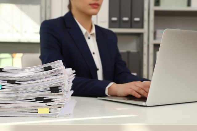Female worker working with laptop near stack of documents in office, closeup